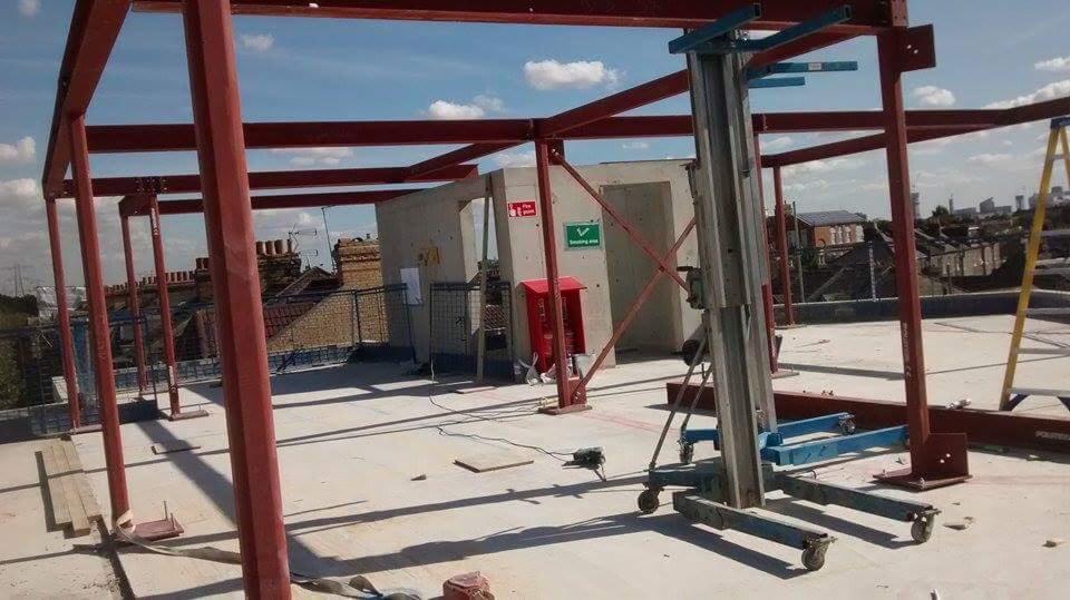 Stalowa konstrukcja szkieletowa w trakcie montażu na dachu budynku, widoczny podnośnik i elementy zabezpieczeń