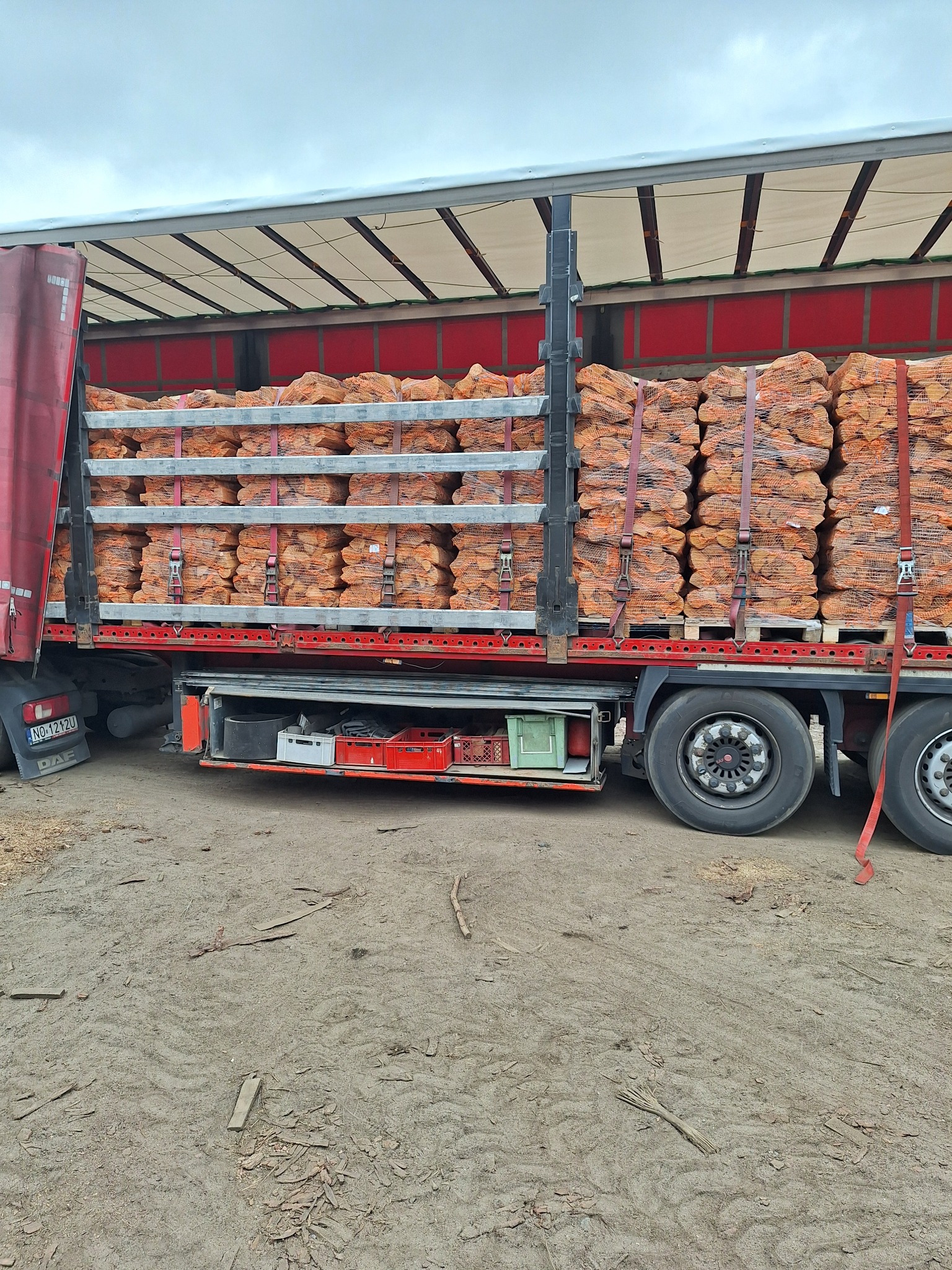 Ciężarówka z plandeką załadowana workami z pociętym drewnem, zabezpieczonymi pasami transportowymi, na terenie składu w Pieniężnie.