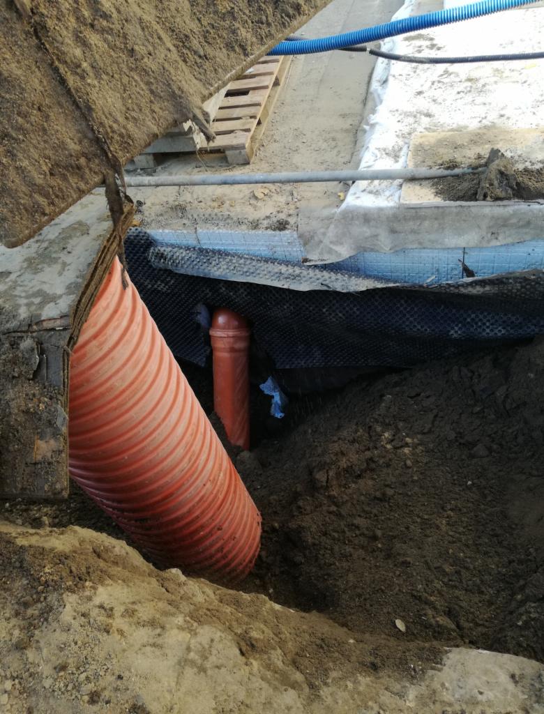 Wykonanie wykopu pod instalację rur kanalizacyjnych z widoczną hydroizolacją i fragmentem szalunku.