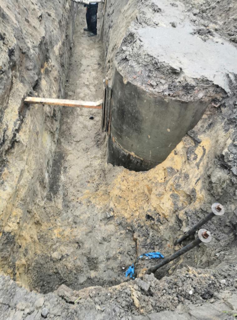 Montaż betonowego szamba w wykopie, widoczne zabezpieczenia ścian wykopu, wystające śruby kotwiące.