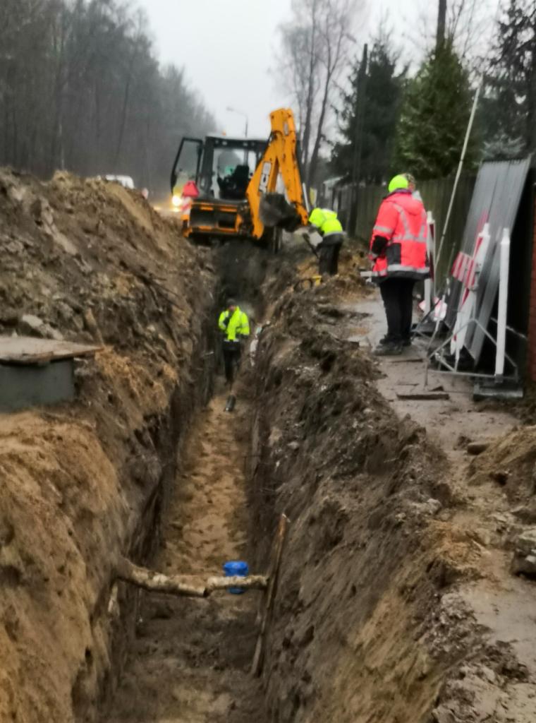 Wykop pod przyłącze w Nowym Mieście, z widoczną rurą i pracującym na miejscu sprzętem ciężkim oraz pracownikami w odblaskowych ubraniach.