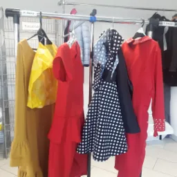 Wieszak na ubrania z różnorodną odzieżą: długa musztardowa sukienka z falbanami, czerwona sukienka z falbanami, sukienka w białe kropki na czarnym tle, czerwona marynarka z ćwiekami na mankietach...