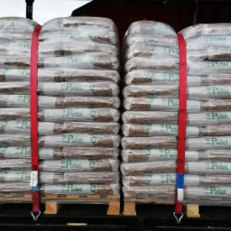 Dwa rzędy palet z workami pelletu zabezpieczone czerwonym pasem transportowym, widoczne drewniane palety i etykiety worków z napisem 'Pellet'.