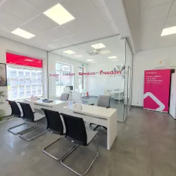 Jasne, nowoczesne biuro agencji nieruchomości z przeszklonymi ścianami, biurkami i krzesłami dla klientów, w oknie plakaty z ofertami mieszkań, a w tle widoczny roll-up reklamowy.