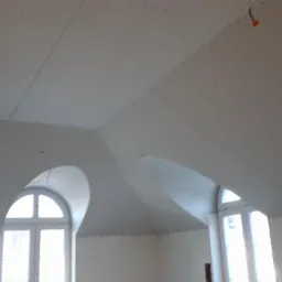 Poddasze z oknami łukowymi w trakcie wykańczania, widoczne płyty na skosach sufitu, przygotowane do dalszych prac wykończeniowych.