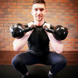 Mężczyzna w czarnym stroju sportowym wykonuje przysiad z dwoma kettlebellami trzymanymi na ramionach na tle ceglanej ściany.