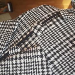 Dorota Grzelak Atelier Projektowo-Krawieckie - Fragment marynarki w pepitkę z czarną lamówką przy klapie, widoczny fragment podszewki w dolnej części kadru.