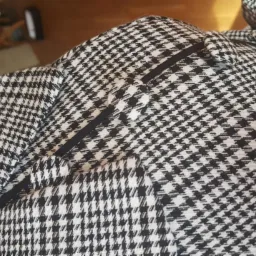 Fragment marynarki w pepitkę z czarną lamówką przy klapie, widoczny fragment podszewki w dolnej części kadru.