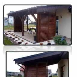 Drewniana konstrukcja z żaluzjowymi ścianami, prawdopodobnie pawilon ogrodowy, z meblami ogrodowymi wewnątrz, otoczona ozdobnymi kamieniami i roślinami, przylegająca do budynku mieszkalnego.