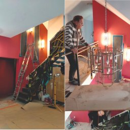 Project Group - Marzenna Cichocka - Dwuczęściowe zdjęcie wnętrza w trakcie aranżacji: czerwone ściany, schody z metalową balustradą, lampy ścienne i sufitowe. Widoczne narzędzia i ekipa remontowa.
