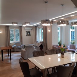Project Group - Marzenna Cichocka - Pałacowy salon po remoncie: parkiet w jodełkę, szare meble, designerskie lampy wiszące. Widok na okna z roślinami. Styl glamour w Zalesiu Dolnym.
