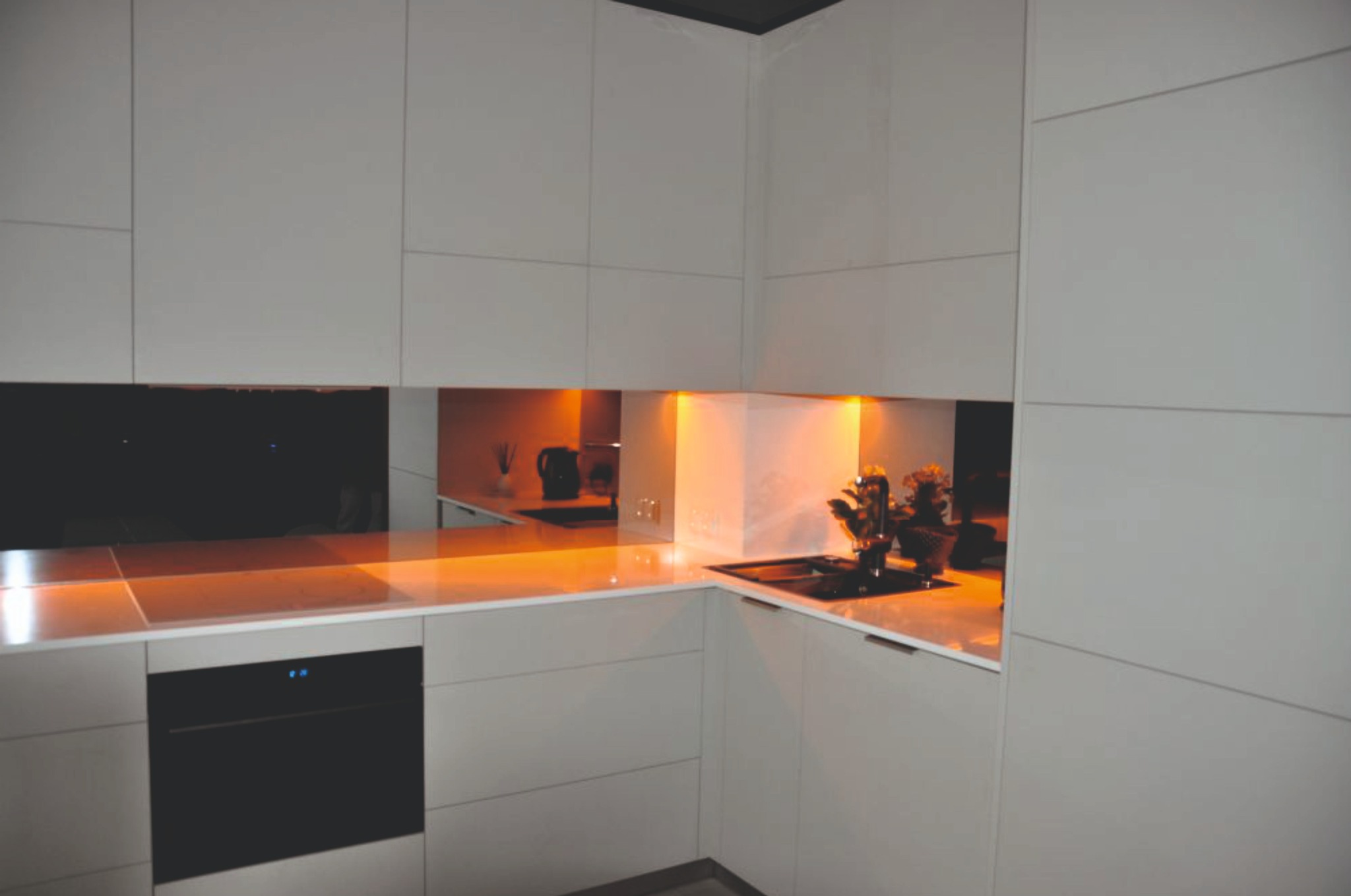 Minimalistyczna kuchnia w odcieniach szarości z podświetlanym blatem i czarnym piekarnikiem. Nowoczesny design z gładkimi frontami szafek i lustrzanymi wstawkami.