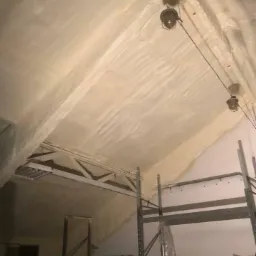 Poddasze po termoizolacji, widoczne metalowe regały i lampy wiszące, nierównomierna powierzchnia izolacji.