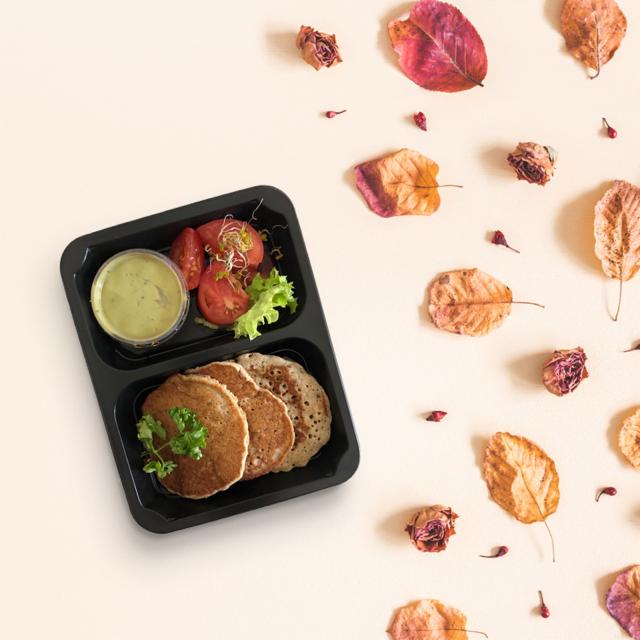 Dietetyczny lunchbox z naleśnikami, pomidorami i sosem, oferowany w Warszawie, na jasnym tle z jesiennymi liśćmi i płatkami róż.