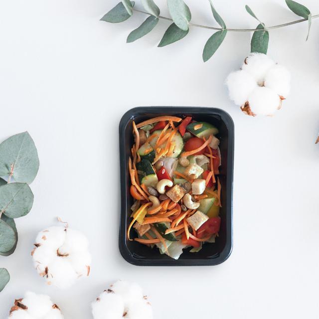 Sałatka warzywna z orzechami i grzankami w czarnym pojemniku, otoczona gałązkami eukaliptusa i kwiatami bawełny na białym tle, widok z góry.