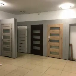 Ekspozycja kilku modeli z przeszkleniami w salonie sprzedaży, widoczna drabina oparta o ścianę.