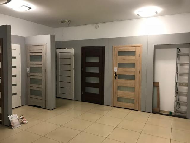 Ekspozycja kilku modeli z przeszkleniami w salonie sprzedaży, widoczna drabina oparta o ścianę.