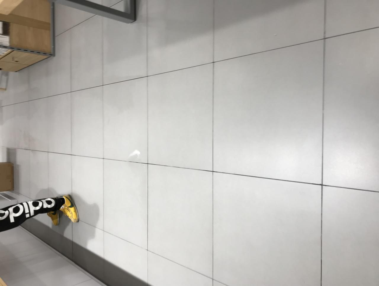 Białe płytki podłogowe w biurze z widocznymi nogami w czarnych legginsach Adidas i żółtych butach sportowych.