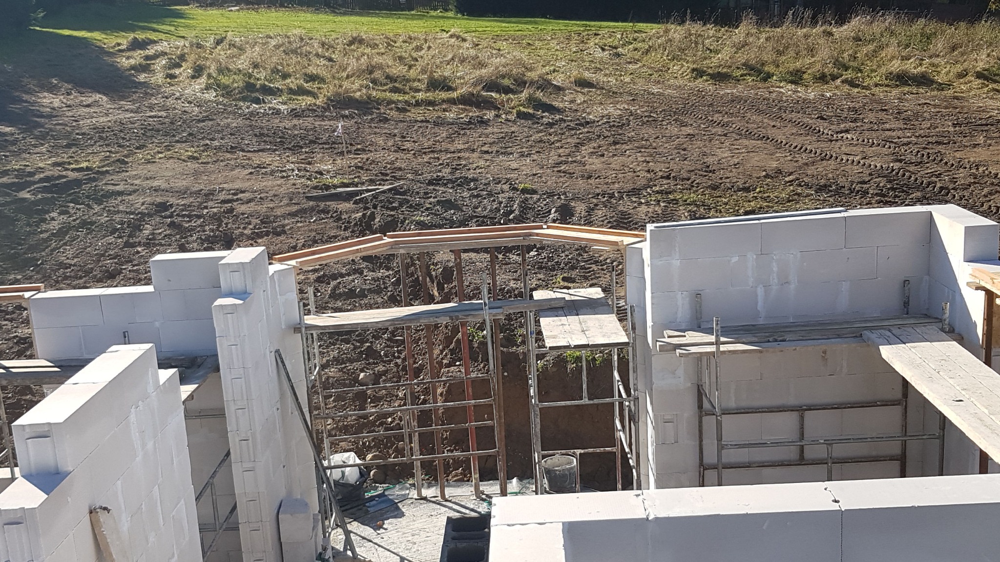 Wznoszenie ścian parteru z betonu komórkowego na fundamencie, widoczne rusztowanie i teren budowy w tle.