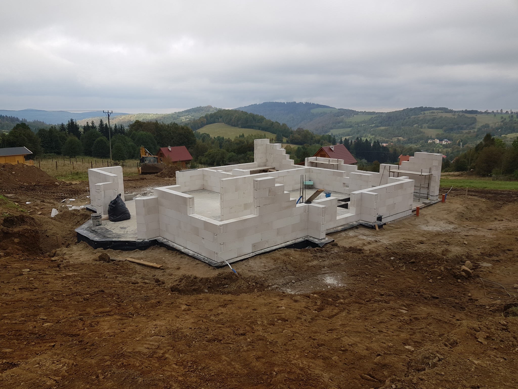 Budowa domu murowanego z bloczków betonu komórkowego na fundamencie, widok na górzysty krajobraz w pochmurny dzień.