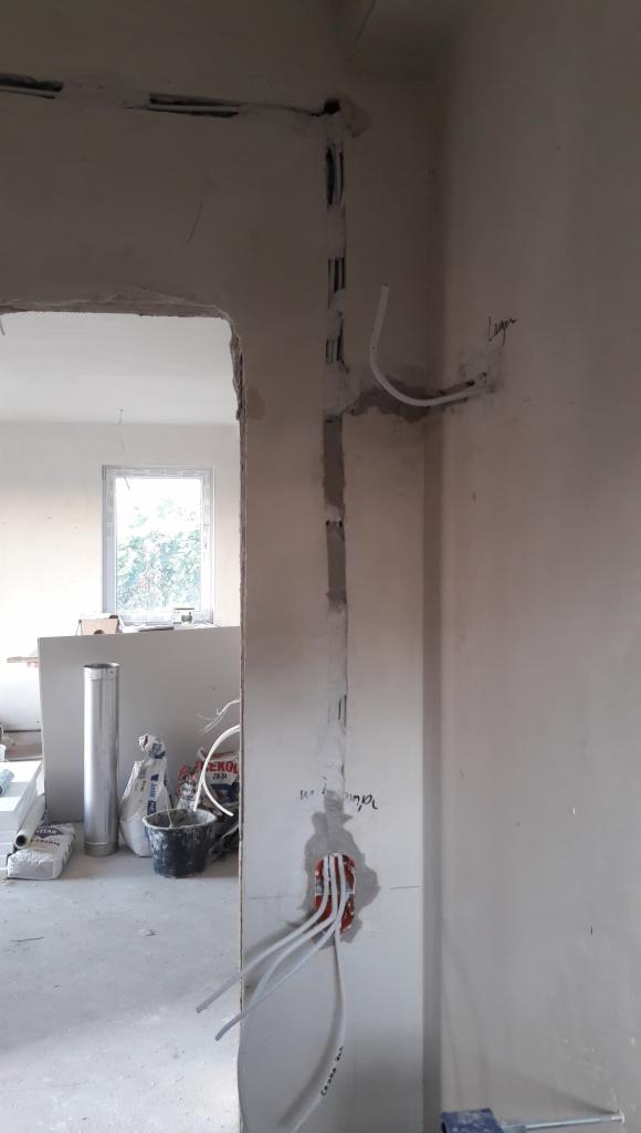 Wnętrze w trakcie remontu: bruzdy pod kable w ścianie, puszka instalacyjna z wyprowadzonymi przewodami, worki z materiałami budowlanymi w tle.