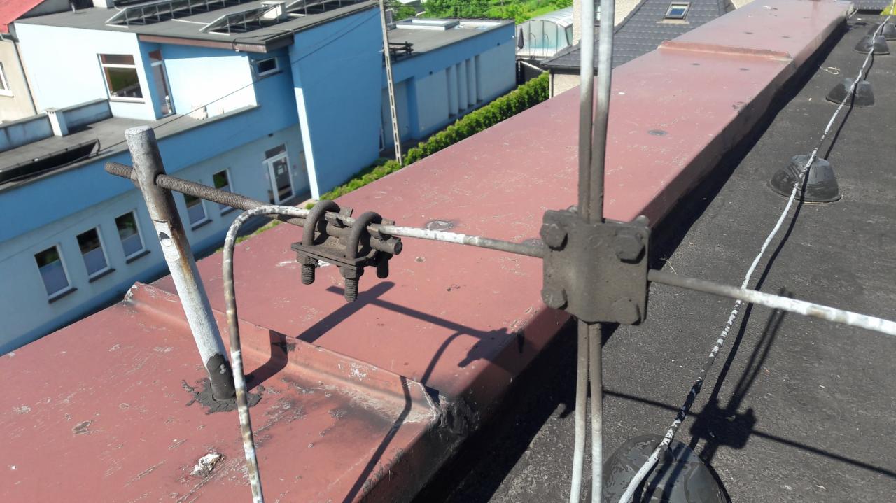 Instalacja odgromowa na dachu budynku w Chorzowie, widoczne metalowe elementy mocujące i przewody uziemiające.