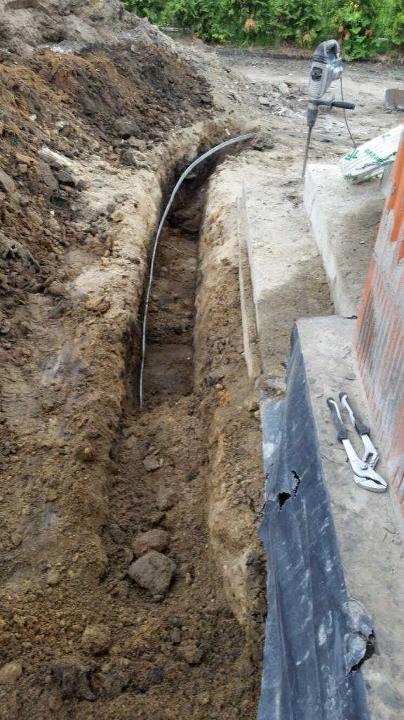 Wykop w ziemi z ułożoną rurą osłonową kabla, obok leżą kombinerki, a w tle widoczny młot udarowy na betonowej powierzchni.