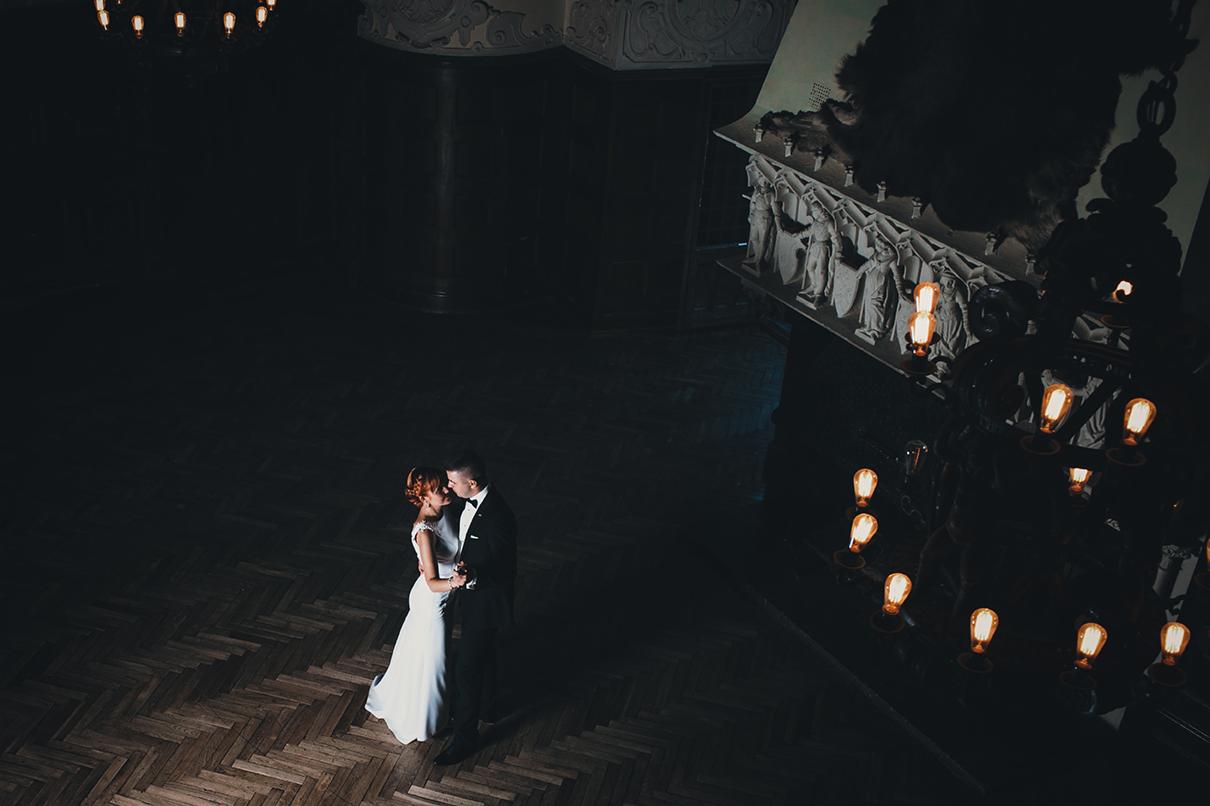 Para młoda w ciemnym, eleganckim wnętrzu z parkietem w jodełkę, oświetlona ciepłym światłem lamp, widok z góry.