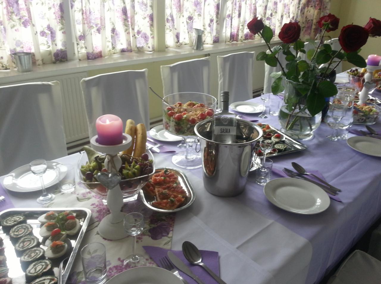 Uroczysty stół z fioletowym obrusem, dekorowany bukietem czerwonych róż, świecą, salaterkami z sałatkami, przekąskami na srebrnych tacach i schłodzoną butelką w wiaderku z lodem, przygotowany...