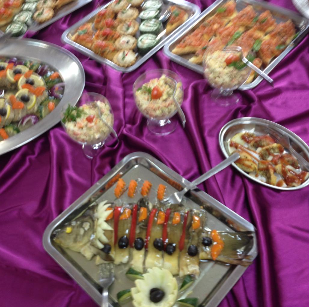Uroczysty stół cateringowy w Radomiu, nakryty fioletowym obrusem, z różnorodnymi przystawkami i daniami, w tym karp w galarecie, sałatki w szklanych naczyniach i kanapeczki na srebrnych tacach.