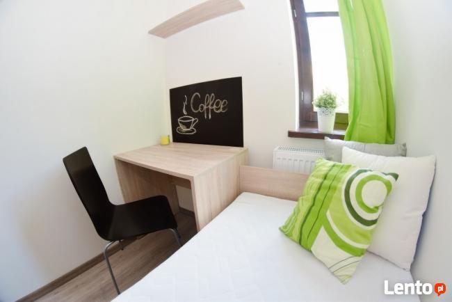 Pokój z biurkiem, krzesłem, łóżkiem jednoosobowym, zielonymi zasłonami i tablicą z napisem 'Coffee' narysowanym kredą.