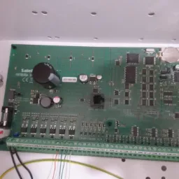 Płyta główna systemu alarmowego Satel Integra 6 zamontowana w białej obudowie, z widocznymi elementami elektronicznymi i podłączonymi przewodami.