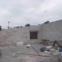 Budowa ścian z bloczków betonowych, widoczna zbrojenie, podpory drewniane, pustak okienny i materiały budowlane na placu budowy.