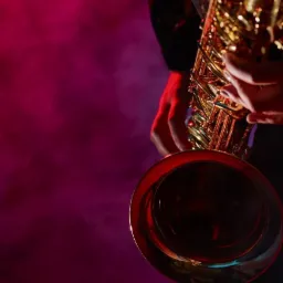 Złoty saksofon w dłoniach muzyka, oświetlony czerwonym światłem na tle dymu.