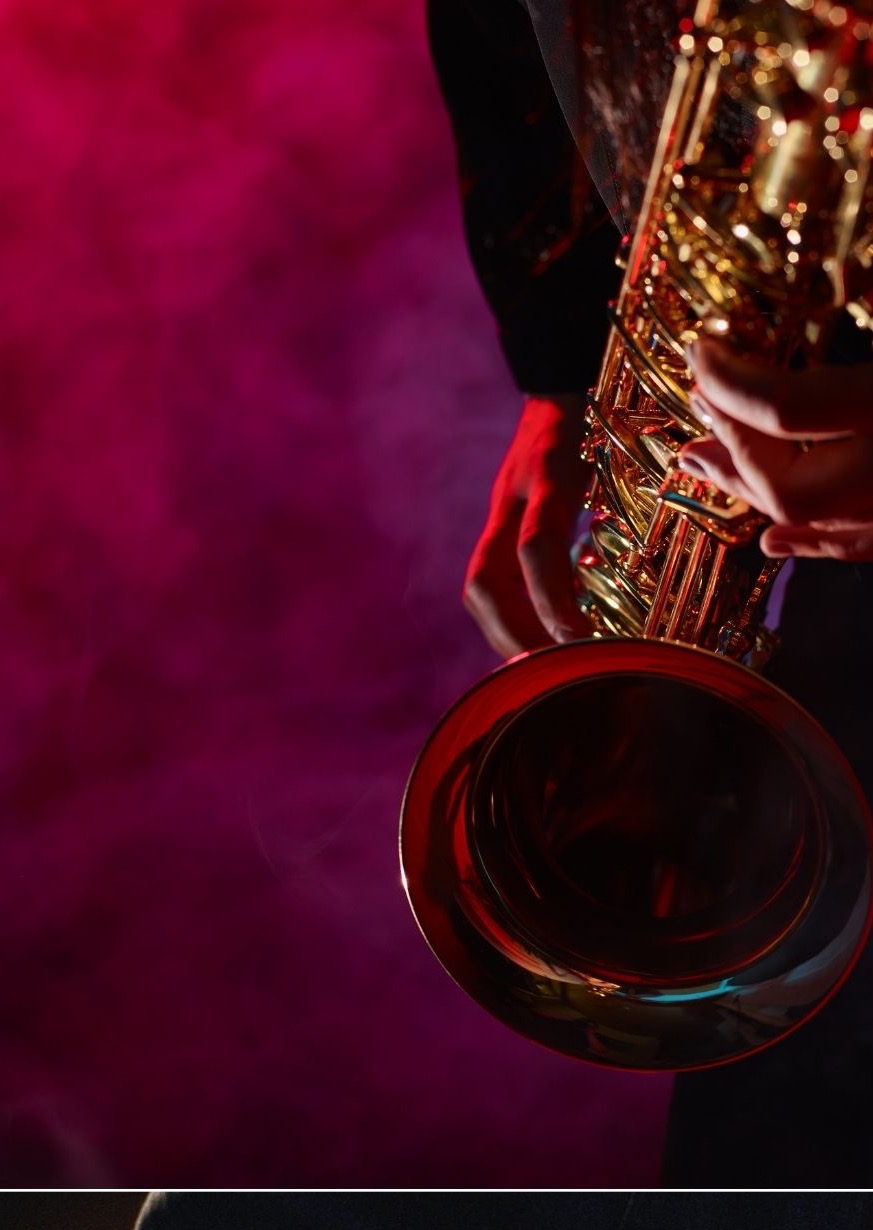 Złoty saksofon w dłoniach muzyka, oświetlony czerwonym światłem na tle dymu.