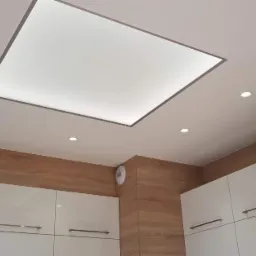 Sufit podwieszany z oświetleniem LED w kształcie kwadratu, uzupełniony punktowymi lampami halogenowymi, w kuchni z białymi szafkami i drewnopodobnymi panelami ściennymi.