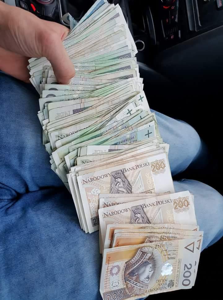 Stos banknotów 200 zł w ręce na tle dżinsów i wnętrza samochodu, prawdopodobnie zapłata za wykonaną usługę budowlaną lub remontową.