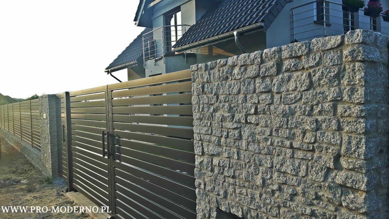 Nowoczesna brama wjazdowa z poziomych profili stalowych, zamontowana pomiędzy kamiennymi słupkami z jasnego granitu, na tle domu z ciemną dachówką.