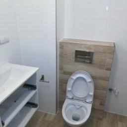 J@P - Nowoczesna łazienka z białymi płytkami ściennymi i beżowymi płytkami podłogowymi, wisząca toaleta z zabudowaną spłuczką, biała szafka pod umywalką z otwartymi półkami.