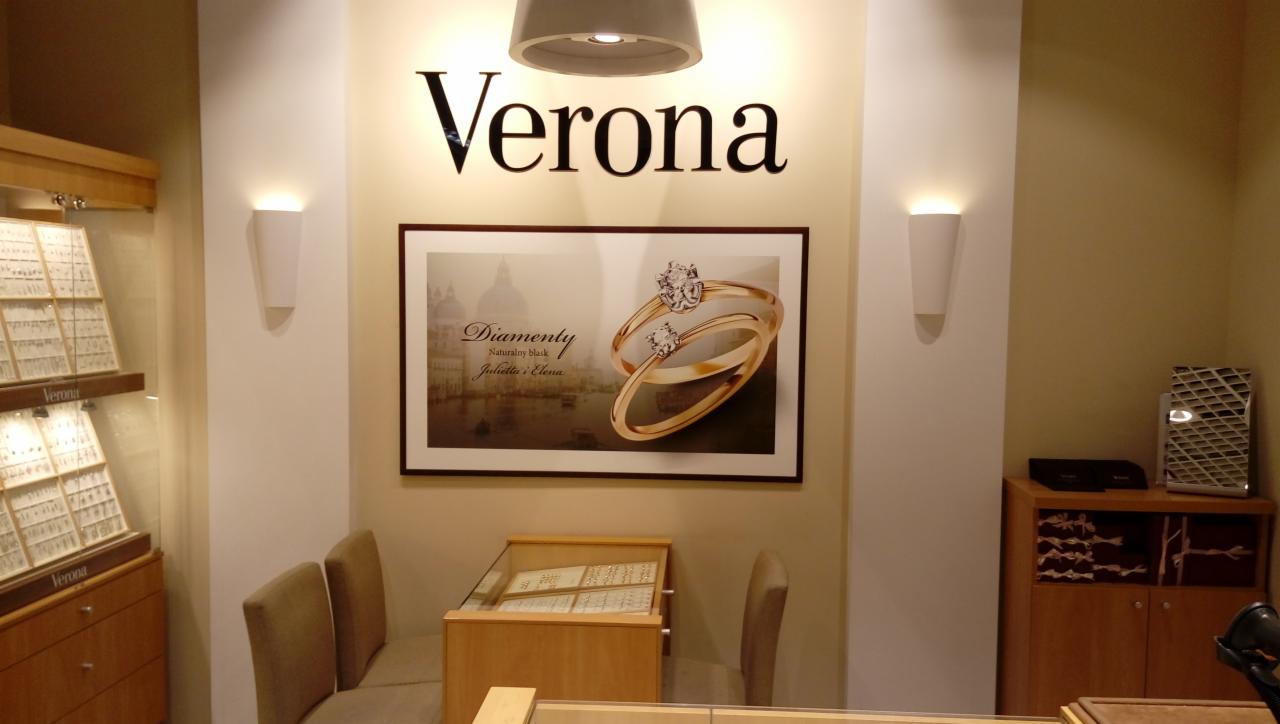 Wnętrze salonu jubilerskiego Verona z ekspozycją biżuterii w gablotach, plakatem z pierścionkami diamentowymi i oświetleniem punktowym.