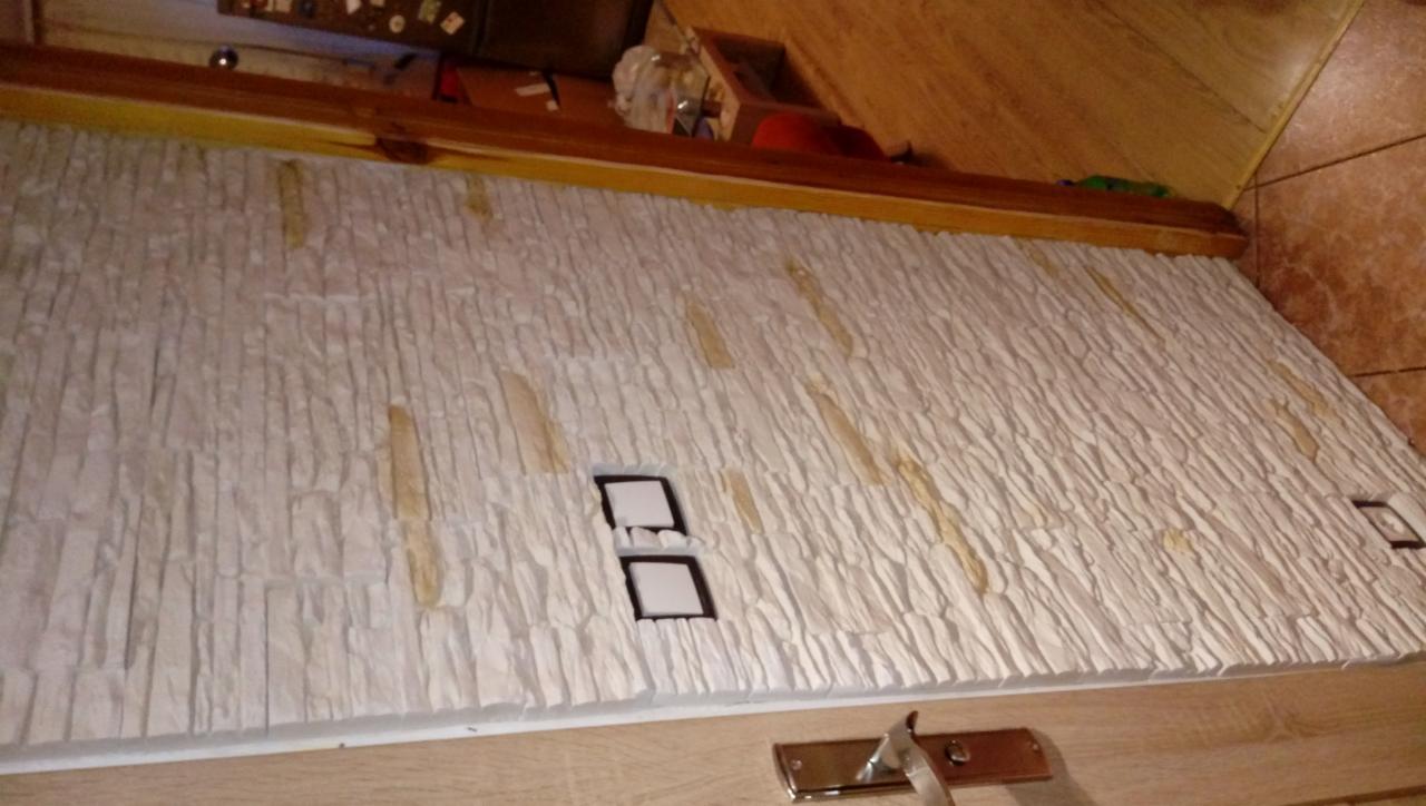 Fragment ściany wykończonej dekoracyjnym kamieniem gipsowym, z widocznymi śladami kleju i dwoma otworami na gniazdka elektryczne, w trakcie prac wykończeniowych.