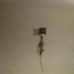 Ściana w pokoju po nałożeniu jasnej struktury, widoczny kabel wystający ze ściany i brązowe drzwi po prawej stronie.