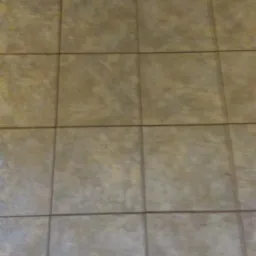 Beżowe, kwadratowe płytki podłogowe z subtelnym wzorem i ciemnymi fugami, ułożone w regularną siatkę.