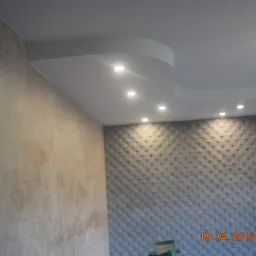 Wykończony sufit podwieszany z oświetleniem punktowym w pomieszczeniu w Żórawiach, widoczna dekoracyjna ściana z trójwymiarową teksturą i fragment ściany pokrytej farbą strukturalną.