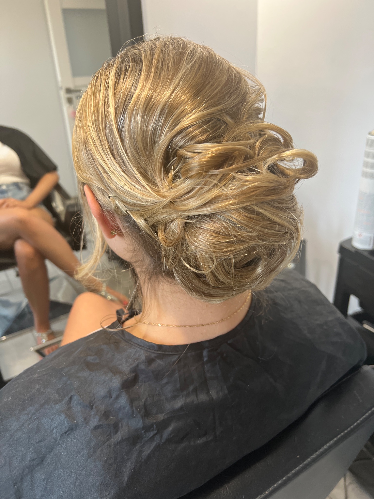 Upięcie ślubne z blond włosów z widocznymi wsuwkami, wykonane w salonie, widok z tyłu.