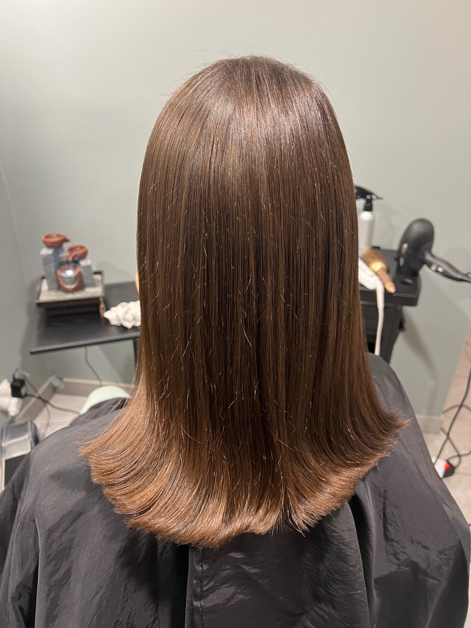 Widok z tyłu na świeżo ostrzyżone, gładkie, brązowe włosy do ramion, z delikatnym podwinięciem końcówek, na tle minimalistycznego wnętrza salonu.