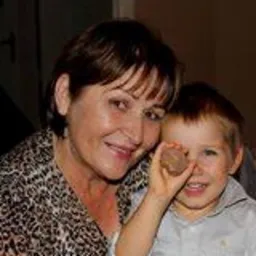 Uśmiechnięta kobieta w bluzce w panterkę i mały chłopiec trzymający orzecha włoskiego przed okiem.