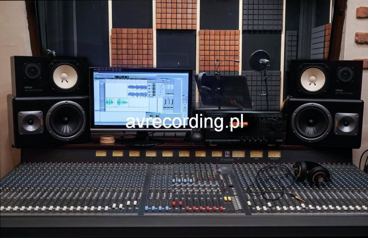 Profesjonalny mikser audio z dużą ilością suwaków i pokręteł, monitory studyjne Yamaha NS-10M Studio, ekran komputera z oprogramowaniem do edycji dźwięku i panele akustyczne na ścianie.