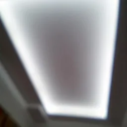 Podwieszany sufit z oświetleniem LED w kształcie prostokąta, wykonany w Łańcucie, z rozmytym tłem i widocznymi fragmentami ściany i mebli.