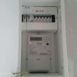 Otwarta skrzynka elektryczna z zamontowanym licznikiem energii i zabezpieczeniami, widoczna ściana w trakcie remontu.